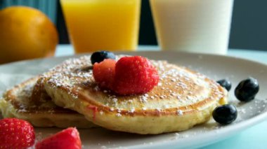 Güneşin ilk ışınlarında kahvaltı, portakal suyu ve ballı krep. Bir kadın büyük bir parça keser. Tabakta kiraz meyvesi var. Yüksek kalite 4k görüntü