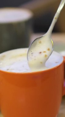 Kadın misafir, kaşık kaşık kremalı kahveyi, güneş ışığıyla aydınlatılarak karıştırıyor. Kırsal ahşap tezgahta kafein ve kek sipariş eden bir bayan. Sabah titreşimleri. Yüksek kalite 4k görüntü
