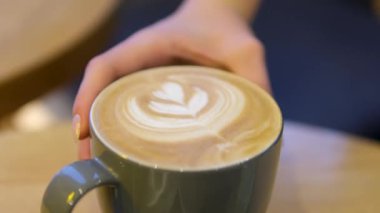 Kadınların elleri bir fincan kahve alır ve masanın üzerine kaldırır, köpüğe Rosetta resmi çizilir. Süt köpüğünden yapılan ince ve kısa ömürlü bir sanat olan lezzetli bir içecek. Yüksek kalite 4k görüntü