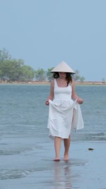 Kadın gezgin, körfezdeki gizli kumsalda tek başına yürüyor. Kumsal ve turkuaz su denizi. Phu Quoc Vietnam 'ın doğası. Vietnam şapkası.