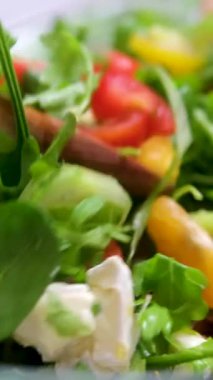 Ahşap bir kaseye taze bir salata atan ellerin yakın çekimi. İtalyan salatasına serpiştirilmiş zeytinyağı