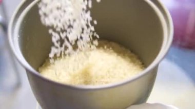 Pirinç Tanesi pilav tenceresine dökülüyor. Mutfakta da ölçü kabı var. Arkasında açık pirinç taneciği kabı var. Yüksek kalite 4k görüntü