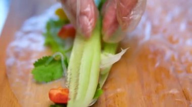 Suşi şefinin yan görüntüsü. Japon üçgenini pirinç kağıdına çeviren eller, yakın plan, taze sebzeler ve otlarla mutfak işyeri. Yüksek kalite 4k görüntü