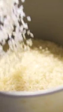 Pirinç Tanesi pilav tenceresine dökülüyor. Mutfakta da ölçü kabı var. Arkasında açık pirinç taneciği kabı var. Yüksek kalite 4k görüntü