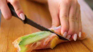 Suşi şefinin yan görüntüsü. Japon üçgenini pirinç kağıdına çeviren eller. Yakın plan, mutfak işyeri. Havuç, kırmızı balık biber ve salatalık sebzeli börek pişir.