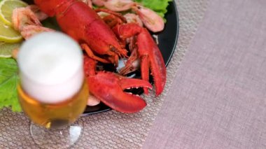 Bir bardak bira kırmızı ıstakoz ezilmiş buz üzerinde limonlu ve yanında limonlu. Taze, sulu ıstakoz kavramı masada tropikal meyve maaşlarıyla lüks bir şekilde sunuluyor. 