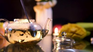 Çay demle. Çerçevede mumlar var, mavi arkaplan karşısında loş ışıkta, cam çaydanlıkta yeşil bir Çin çayı. Rahatlama ve sükunet kavramı. Yüksek kalite 4k görüntü