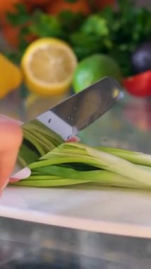 Kadınların elinde bıçak, tahta kesme tahtasındaki taze Japon soğanlarını kesiyor. Tahta bir tahtanın üzerinde dilimlenmiş pırasa ya da doğranmış yeşil Japon soğanı. Yüksek kalite 4k görüntü