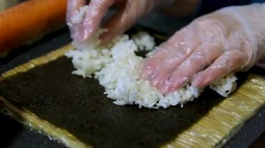 Suşi çekim yapıyor. Deniz yosunu. Siyah eldivenli şef deniz ürünleri suşisi hazırlar. Somon ve avokado ile suşi rulo. Lezzetli Japon yemekleri. 4 bin. Kapatın. Yüksek kalite 4k görüntü