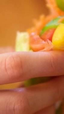 Suşi şefinin yan görüntüsü. Japon üçgenini pirinç kağıdına çeviren eller. Yakın plan, mutfak işyeri. Havuç, kırmızı balık biber ve salatalık sebzeli börek pişir.