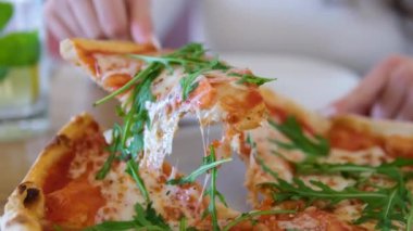 Kız bir dilim pizza alır ev yapımı pizza üzerine roka, domates dilimleri ve peynirle kaplanmış, pişirme malzemeleriyle çevrili. Yüksek kalite 4k görüntü