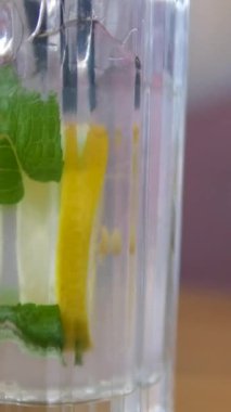 Bir insan kevaşe içindeki parlak limonlarla çevrili bir tabağa taze limon suyu sıkıyor. Nane yaprakları renk katar, ev yapımı narenciye için canlı ve sağlıklı bir ortam yaratır. 