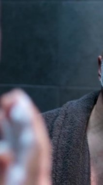 Aynanın yanındaki duş kaplıcalarından sonra bornozlu bir adam banyoda aynanın yanındaki banyoda tıraş olur, cilt bakımı yapar. Yüksek kalite 4k görüntü