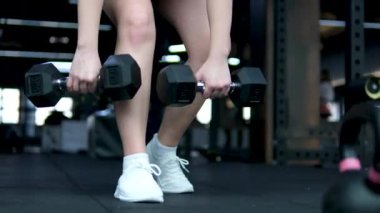 Spor eğitmeni ışık stüdyosunda dambıl çömelmesi yapıyor. Kasları iyi tanımlanmış güçlü bir kadın spor salonunda güç ve teknik gösterisi yapıyor. Harekete geçen motive bir kadın. 