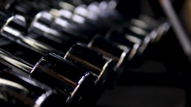 Spor salonunda ağırlık rafları ve arka planda görünen banklar gibi dayanıklılık eğitimi ekipmanlarıyla düzenli halterlerin sıra sıra odak çekimini yapın. Yüksek kalite 4k görüntü