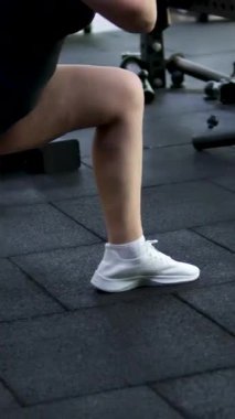 Spor eğitmeni ışık stüdyosunda dambıl çömelmesi yapıyor. Kasları iyi tanımlanmış güçlü bir kadın spor salonunda güç ve teknik gösterisi yapıyor. Harekete geçen motive bir kadın. 