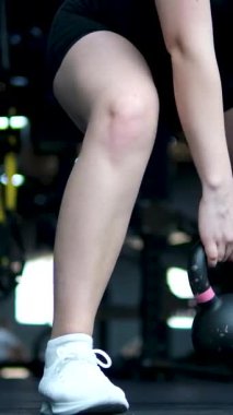 Genç bir kadın spor salonunda kettlebell salıncaklarıyla çalışıyor. Siyah spor giysili çekici güçlü bir kadın. Kettlebell kaldırıyor. Fotokopi uzayı ile orta çekim. Yüksek kalite 4k görüntü
