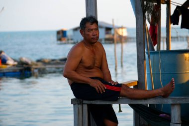Asyalı sakallı bir adam, güzel deniz manzarasının önünde oturuyor, güneşli plajda tek başına dinleniyor. Vietnam Phu Quoc Adası 02.16.2025