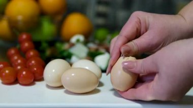 Eller ustalıkla kaynamış yumurtaların kabuklarını soyar ve pürüzsüz beyaz yüzeyi ortaya çıkarır. Yumurta kabukları tezgahın üzerine saçılır, aşçılık hazırlığı ve basitlik duygusu taşır. 4k