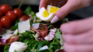 Profesyonel şef renkli domates salatası üzerine kaynamış yumurtaları dikkatlice kesiyor, zarif yavaş çekim videosunda hassas mutfak teknikleri sergiliyor. Yüksek kalite 4k görüntü