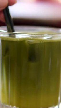 Matcha, beyaz elin yakın çekim videosu yeşil maddeyi karıştırıyor. Portakal suyu ve kibrit çayı. Sağlıklı, portakal suyu ve kiraz yeşili çay.