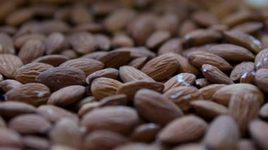 Bademler gri arka plana düşüyor. Badem fıstıkları masaya düşer. Beyaz kaseden gri masaya düşen kahverengi badem fıstıklarının yakın çekimi. Ağır çekim. Dikey video. Yüksek kalite 4k görüntü