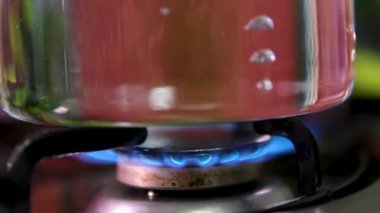 Elektrik ya da indüksiyon sobası parlayan ocağı, küçük paslanmaz bir tencerede kaynar su. Yakın çekim, gerçek zamanlı, insan yok.