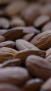 Bademler gri arka plana düşüyor. Badem fıstıkları masaya düşer. Beyaz kaseden gri masaya düşen kahverengi badem fıstıklarının yakın çekimi. Ağır çekim. Dikey video. Yüksek kalite 4k görüntü