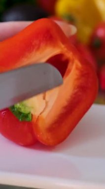 Ahşap tahtada bıçakla taze kırmızı bir dolma biberi kesen şefin ellerini yakın plan çek. Aşçı mutfakta vejetaryen salatası hazırlıyor., 