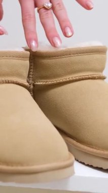 Bej renkli ugglar kız el ele tutuşur. Ayakkabı bacağını beyaz çorapla muayene eder. Ayakkabıları dener. Kadınlar için sıcak deri çizmeler. yeni kış uggları