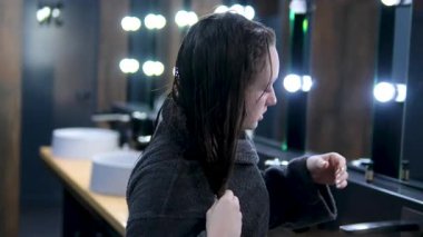 Genç ve güzel bir kadın aynaya bakarken saçını kurutuyor, fön makinesi. Otellerin banyosundaki aynadaki kadın yansıması. Yüksek kalite 