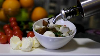 Mutfak masasındaki salataya zeytinyağı ekler. Genç bir kadın mozzarella salatası yapmak için çeşitli sebze ve peynirler kullanarak zeytinyağı döküyor. Yüksek kalite 4k görüntü
