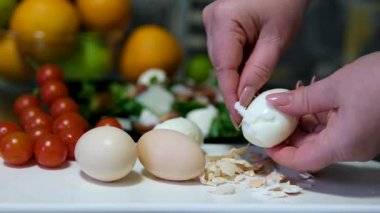 Eller, Mutfak Lavabosunda Bir Kase Su Üzerine Kaynamış Yumurta Dikkatlice Soyar, Ev Mutfağı Ayarlarında Taze İçindekilerle Basit Bir Pişirme Sürecini Gösterir. Yüksek kalite 4k