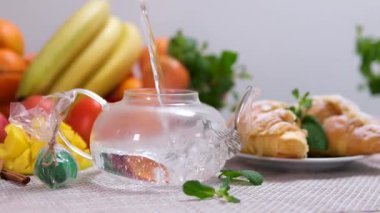 Fresh Fruits 'lu bir mutfakta cam bir çaydanlığa sıcak su dökmek. Yüksek kalite 4k görüntü