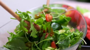 Fresh salad with lettuce leaves and tomato falling into bowl, served with healthy food ingredients on white table, slow motion. High quality 4k footage