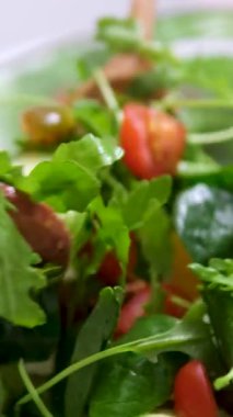 Fresh salad with lettuce leaves and tomato falling into bowl, served with healthy food ingredients on white table, slow motion. High quality 4k footage