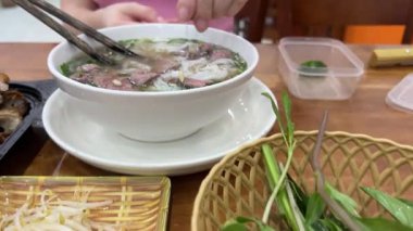 Taze yapılmış pho çorbası fasulye lahanası ve fesleğen yapraklarıyla süslenir. Kadın sıcak Asya çorbasının tadını arttıran malzemeler ekler. Geleneksel Vietnam çorbası, mis kokulu et suyu ve taze bitkilerle. 4k