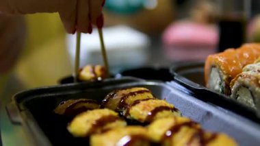 Yosun kaplı pirinç, yosun sarılı pirinç. Adamın eli, arkadaşına ya da mangal arkadaşına yumuşak kabuklu deniz yosununa sarılı pirinç toplamak için tahta çubuklar kullanır. Peynirli suşi.