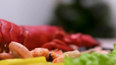 Tahta tahtada sunulan taze ıstakoz, karides ve somonlu gurme deniz ürünleri tabağı, çeşitli sebze ve soslarla tamamlanmış, deniz kenarında lüks yemekler sergileniyor. Güzel yemek deneyimi.