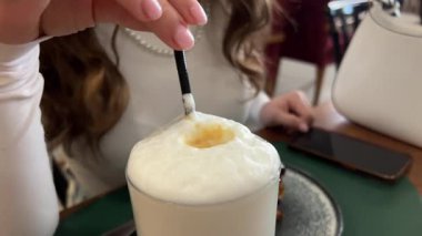 Kadın eli cam bardakta metal kaşıkla cappuccino kahve köpüğü karıştırıyor. Yüksek kalite 4k görüntü