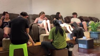 Tayland masaj salonunda yağlı profesyonel ayak masajı. Bulanık arka planda, rahatlatıcı bir koltukta uyuyan genç bir kadınla. Vietnam Danang 04.10.2025