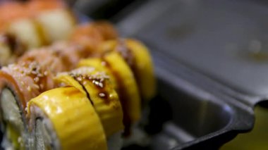 Suşi ruloları ve sashimi, taze somon ve çeşitli malzemelerin yer aldığı beton bir yüzeyde siyah kaplarda çekici bir şekilde sunuluyor. Tütsülenmiş peynir ve mango suşisi