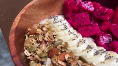 Smoothie, granola, ejderha meyvesi, dilimlenmiş muz, nane, çilek, hindistan cevizi ve yabanmersinli nefis bir tropikal kase. Kadın eli, meyve suyu kasesini kaşıkla karıştırıyor. Mükemmel. 