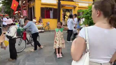 Küçük kız caddenin ortasında fotoğraf çekiyor. Bisikletçi tüccarlar Hoi An City Vietnam 'ın yanında duruyorlar. 05.02.2025