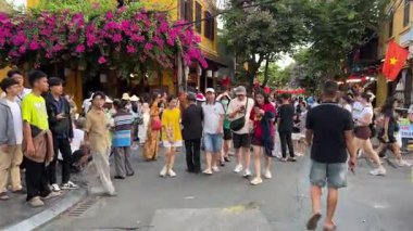 Bir grup turist caddelerde yürüyor, triportörler müşterileri bekliyor, insanlar fotoğraf çekiyor, sarı evleri görüyorlar Hoi An Şehri Vietnam 05.02.2025