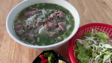 Vietnam pho çorbası aromatik et suyu, pirinç eriştesi ve taze otlar. Kültürel gelenek ve sağlıklı yemek deneyimi sergileyen lezzetleri geliştirmek için fesleğen ve limon ekleme süreci..