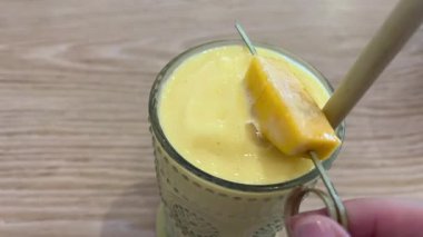 Taze yapılmış sarı turuncu ve mangolu smoothie, güneşli sarı arka plandaki bir şişeden bir bardağa akıyor. Yüksek kalite 4k görüntü