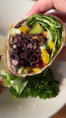 Dişi el burrito tutuyor ve sarı plastik sepetin üzerinde guacamole sosu ile kaplıyor. Kadının elinde soslu vejetaryen burrito tutarken yakın plan fotoğrafı. Geleneksel Meksika mutfağı. Yüksek kalite 4k