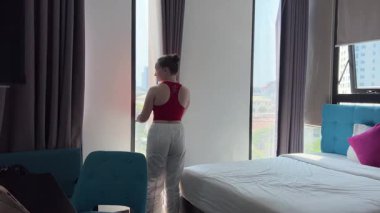 Arkadan bakan mutlu genç kadın perdeyi açıyor lüks bir dairede ya da modern bir otelde tek başına panoramik pencereden bakıyor ve sabah manzaranın keyfini çıkarıyor. Yeni konut, mülkiyet, seyahat.