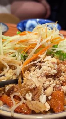 Kadınlar sokak yemeği yemeden önce kaşık ve yemek çubukları ile erişteleri lezzetlerle karıştırırlar. Pirinç vermicelli Papaya salatası, pirinç vermicelli ve mayalanmış balık soslu salata. Yüksek kalite 4k